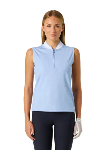 A woman modeling a sleeveless light blue golf polo shirt with a half-zip collar, paired with dark pants and a white glove, against a plain white background.