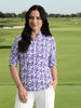 Woman wearing a purple patterned shirt and white pants on a gray background