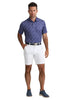 Man wearing a blue patterned polo shirt and white shorts on a white background
