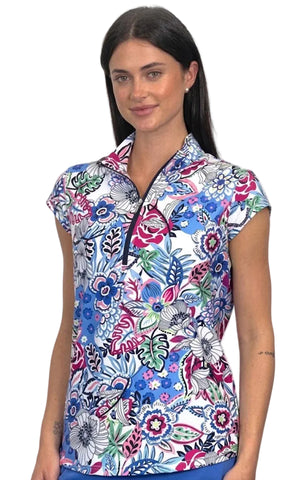 A woman modeling a short-sleeve collared scrub top with a colorful floral and butterfly print on a white background, paired with blue bottoms, against a light gray studio backdrop.