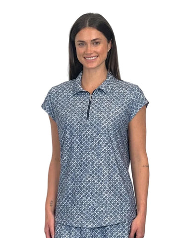 A woman modeling a short-sleeve polo shirt with a blue and white geometric pattern, featuring a half-zip collar, set against a plain white wall.