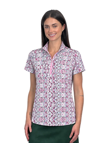 A woman modeling a short-sleeve collared top with a pink, white, and black geometric pattern and a pink zipper at the collar, paired with a dark green skirt, against a plain white background.