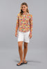 Woman wearing a colorful patterned shirt and white shorts on a gray background