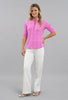 Woman wearing a pink patterned blouse and white pants on a gray background