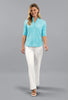 A woman modeling a light blue patterned short-sleeve quarter-zip top with white pants, standing against a solid gray studio background.