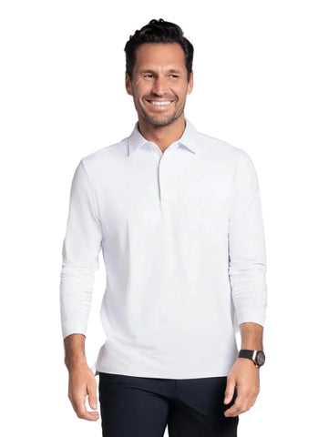 A smiling man wearing a white long-sleeve polo shirt and dark navy shorts, standing against a solid studio background.