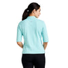 Woman wearing a light blue polo shirt with a visible brand logo on a white background