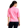 Woman wearing a pink shirt with a visible brand logo on a white background