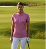 Woman in pink shirt and white pants standing on a golf course with a golf club.