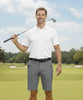 Man holding a golf club on a golf course with trees and sky in the background