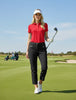 Woman in red shirt and black pants holding a golf club on a golf course